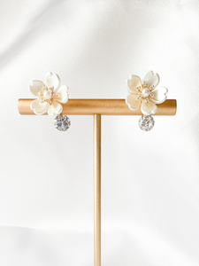 white flower clipon earrings with small cubic zirconia gem dangling on the bottom on T stand