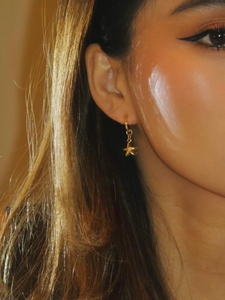 A pair of gold-colored clip-on hoop earrings with star-shaped pendants worn by a model
