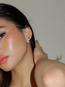 Close-up of a woman's profile showcasing a sparkling flower-shaped earring with multiple gemstones on her earlobe, with a focus on the jewelry against her glowing skin.