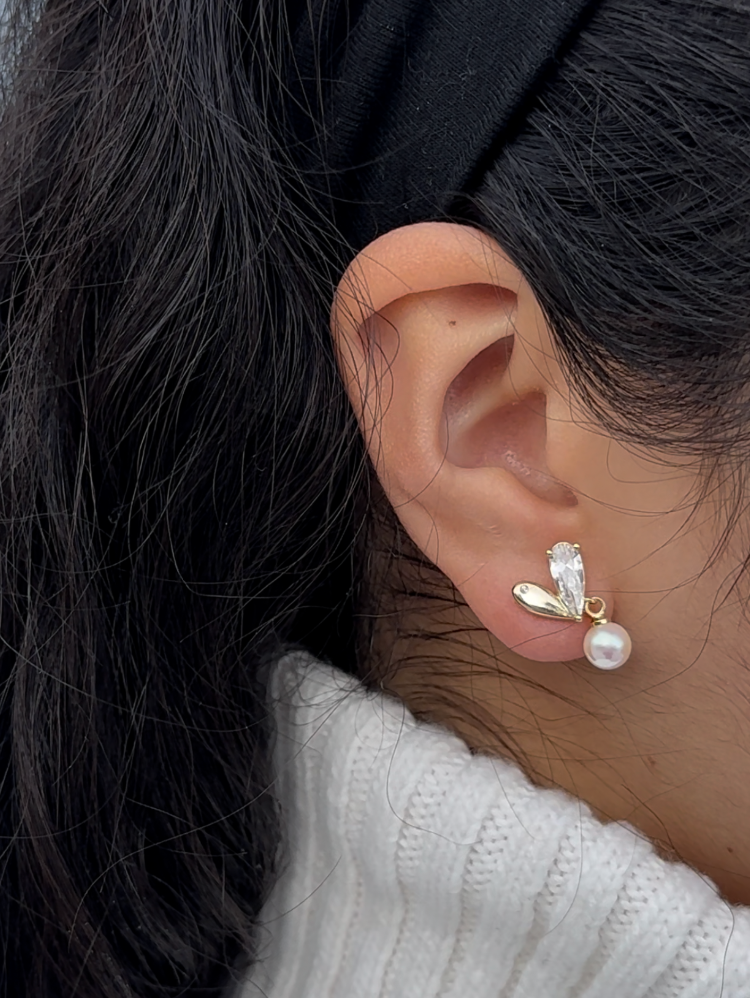 heart shaped clip-on earrings with pearl dangling from half of the heart on model one half of the heart is made up of white cubic zirconia and the other half is gold.