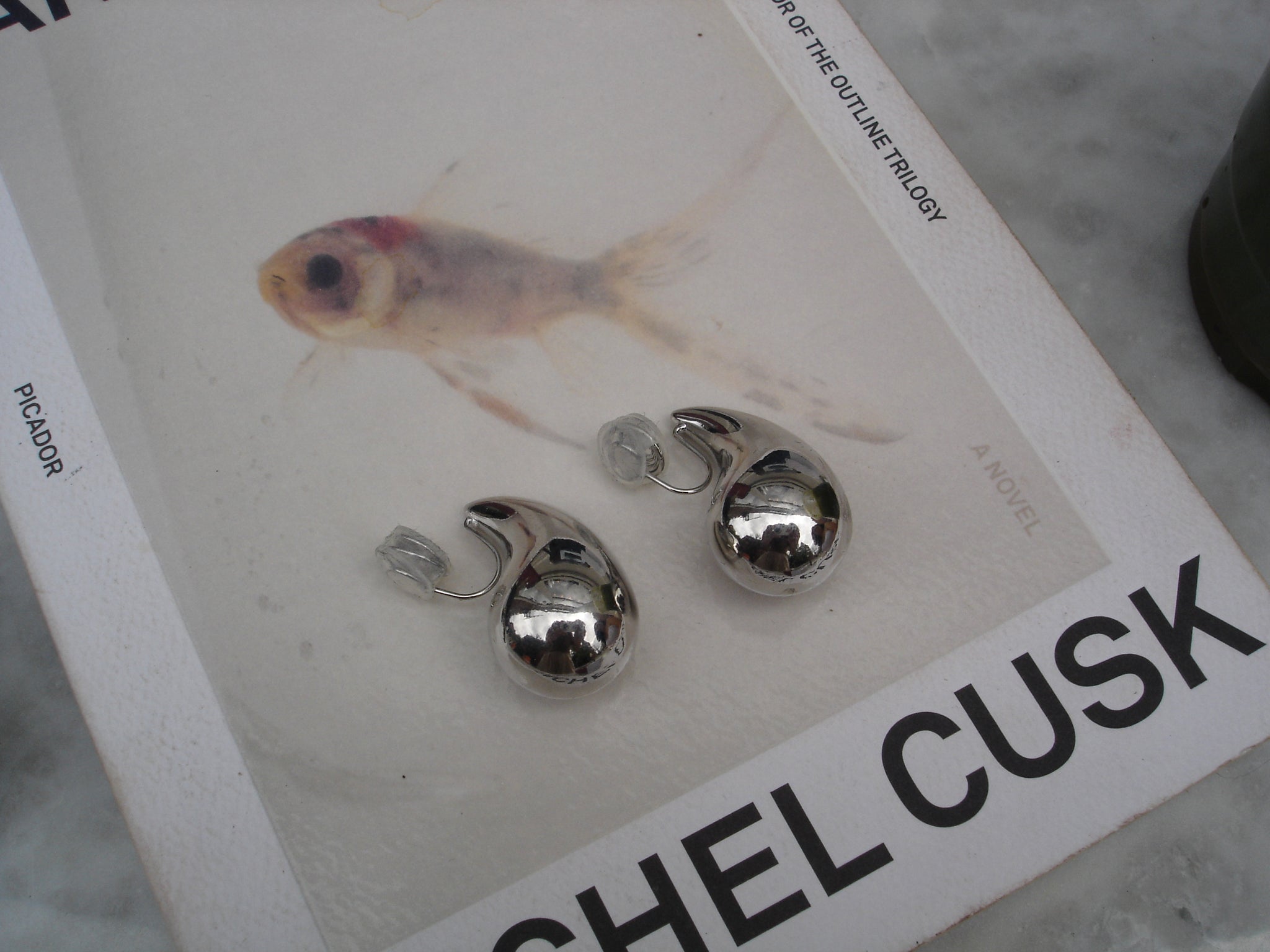 Silver earrings on a book titled 'Shel Cusk' with a fish illustration.