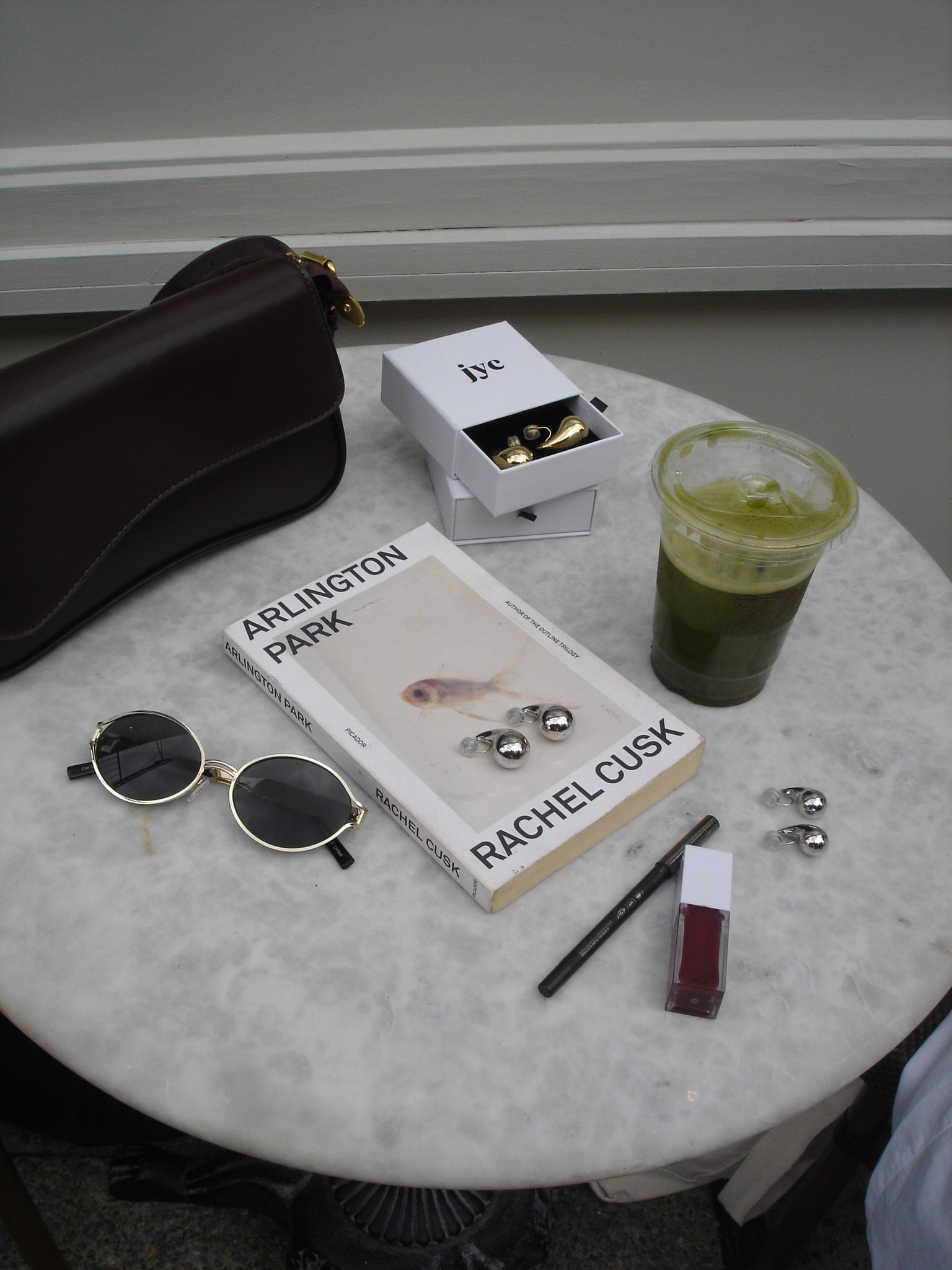 Round marble table with various items including a book, sunglasses, and a green cup.