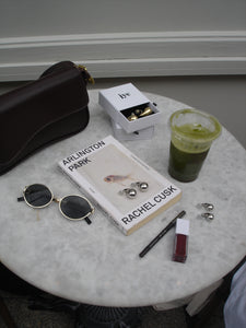 Round marble table with various items including a book, sunglasses, and a green cup.