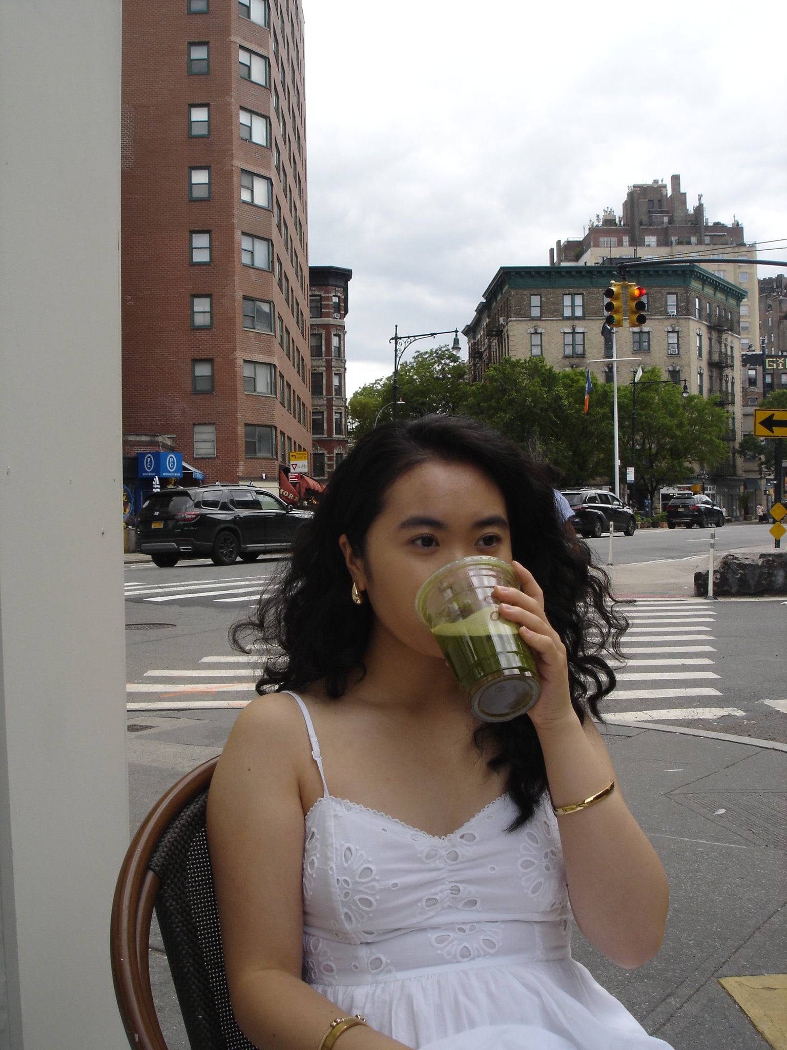 Woman drinking from a bottle on a city street with buildings and traffic lights in the background.