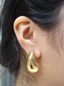 Gold earring worn on an ear with dark hair