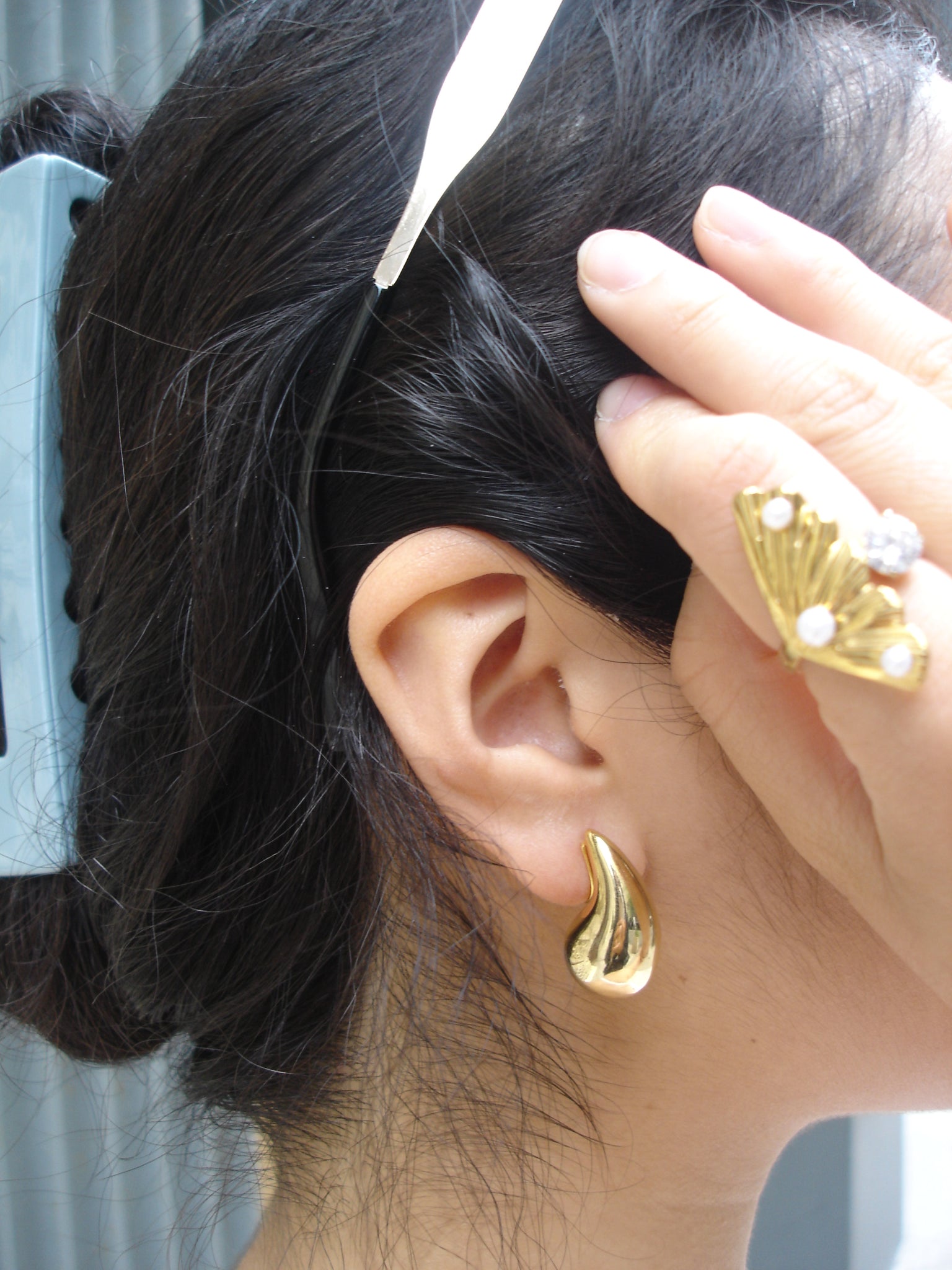 Close-up of an ear with gold earrings and hair being styled.