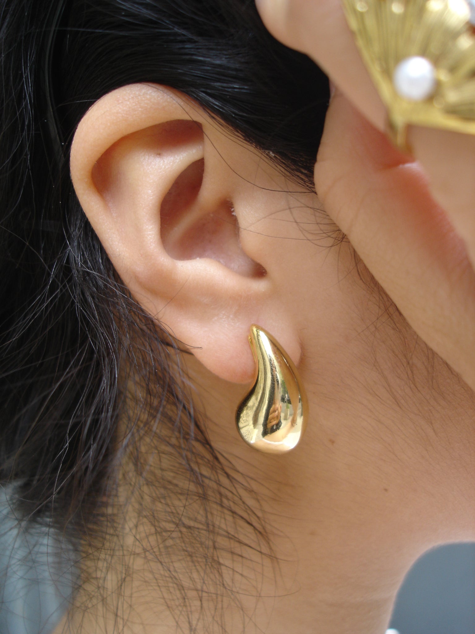 Gold earring worn on an ear with a blurred background
