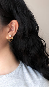 These elegant gold heart clip-on earrings feature a pearl sitting atop the heart-shaped design. The earrings are crafted from high-quality materials and have a secure clip-on mechanism for comfortable wear. Perfect for adding a touch of sophistication to any outfit, these earrings make a great addition to any jewelry collection.