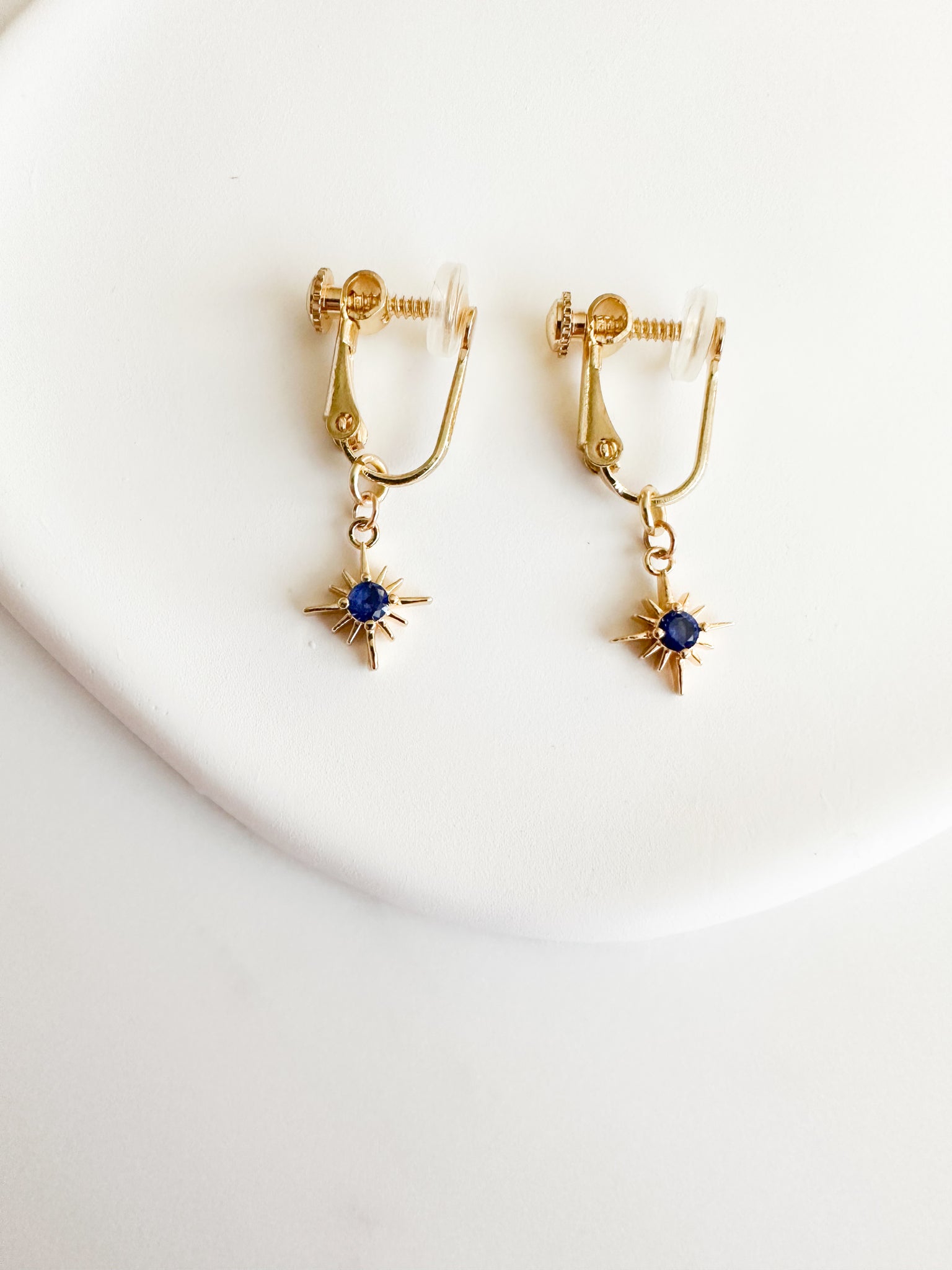 gold screwback clipon earrings with gold constellation charm with dark blue circle gem in middle
