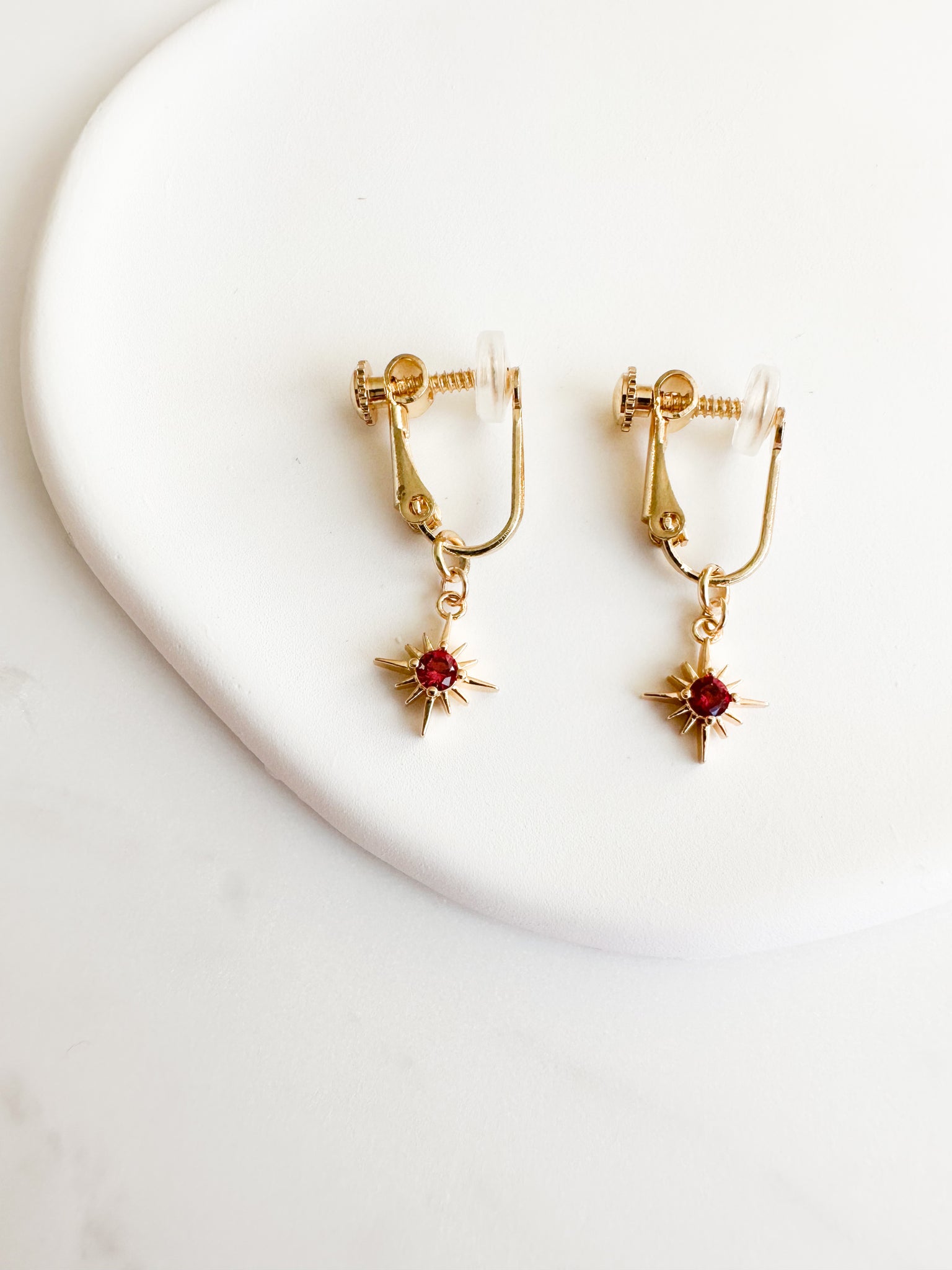 gold constellation charm with a ruby red gem in the middle. screwback clipon earrings