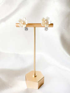 white flower clipon earrings with small cubic zirconia gem dangling on the bottom on T stand