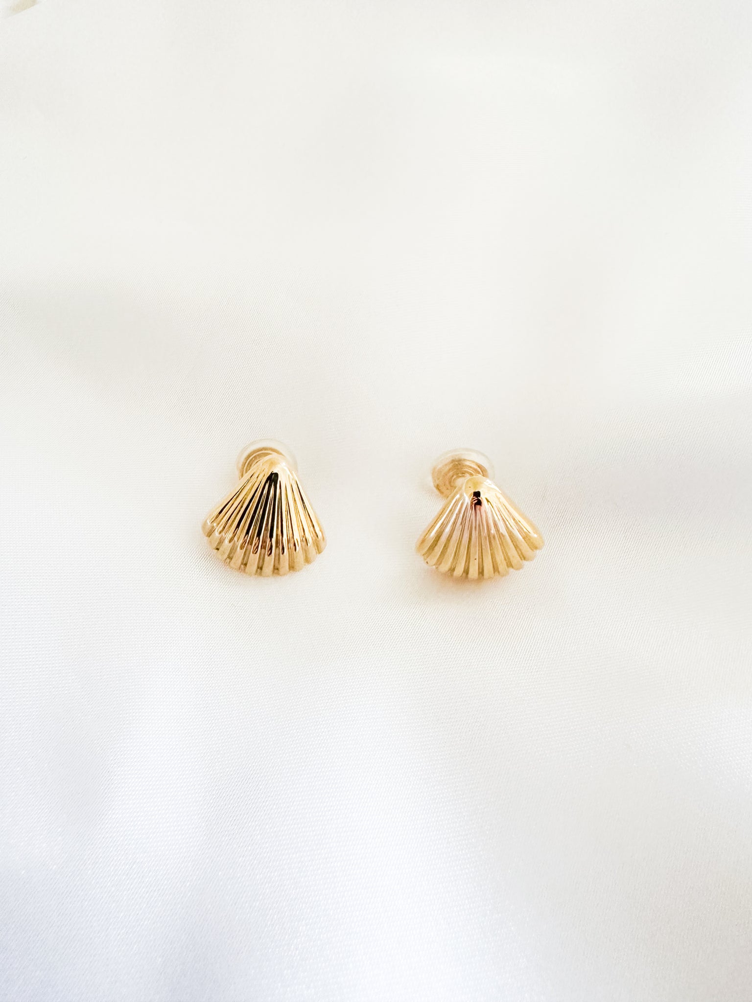 Gold shell-shaped earrings on a light beige background