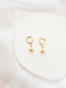 A pair of gold-colored hoop clip-on earrings with star-shaped pendants, displayed on a white surface.