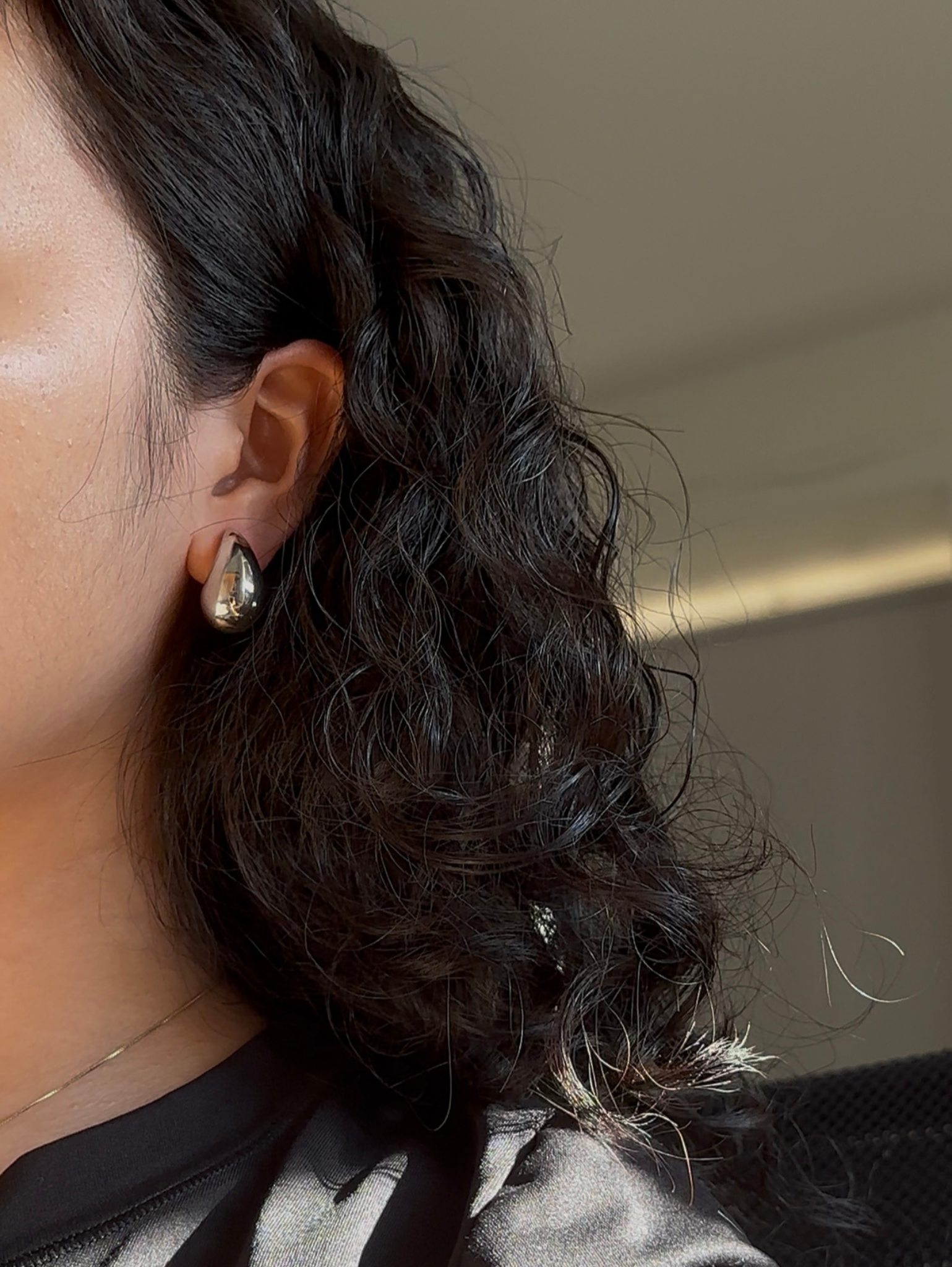 Close-up of a person's ear with an earring, hair styled in loose curls.