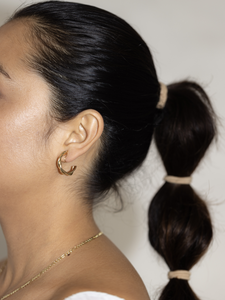 Pair of gold-tone clip-on hoop earrings with a unique twisted design. The earrings feature a hinged back closure that securely clips onto the earlobe, making them easy to wear without the need for pierced ears. The hoops have a shiny gold finish and the twisted design adds a touch of texture and dimension to the classic hoop earring style