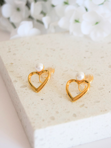 These elegant gold heart clip-on earrings feature a pearl sitting atop the heart-shaped design. The earrings are crafted from high-quality materials and have a secure clip-on mechanism for comfortable wear. Perfect for adding a touch of sophistication to any outfit, these earrings make a great addition to any jewelry collection.