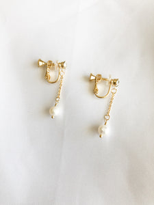 These screwback clip-on earrings feature a gold plated metal base with a cubic zirconia charm hanging from a short dangle pearl. The earrings are designed to be worn without the need for pierced ears. The screwback mechanism ensures a secure and comfortable fit for all-day wear.